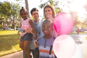 White couple with their black kids smiling and holding balloons