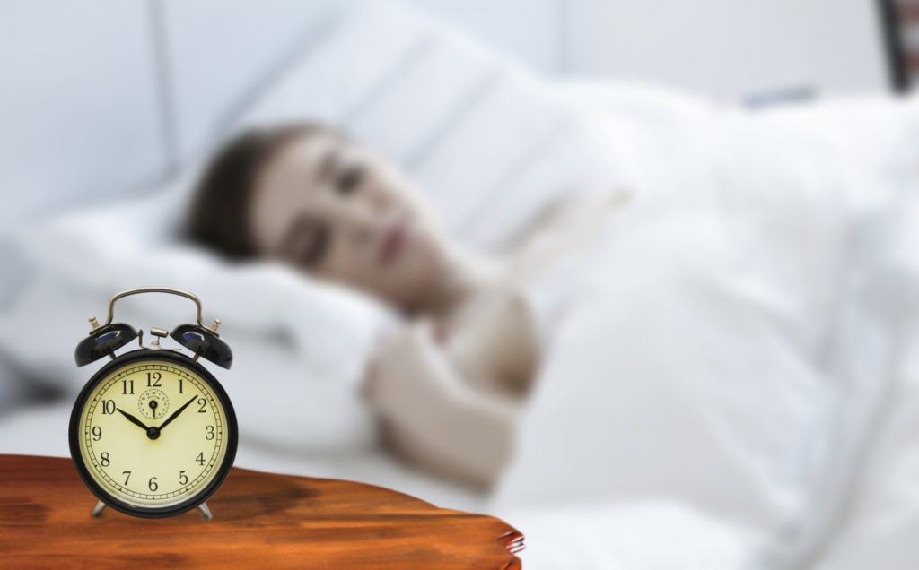 Girl sleeping with a white sheet and an alarm clock on table