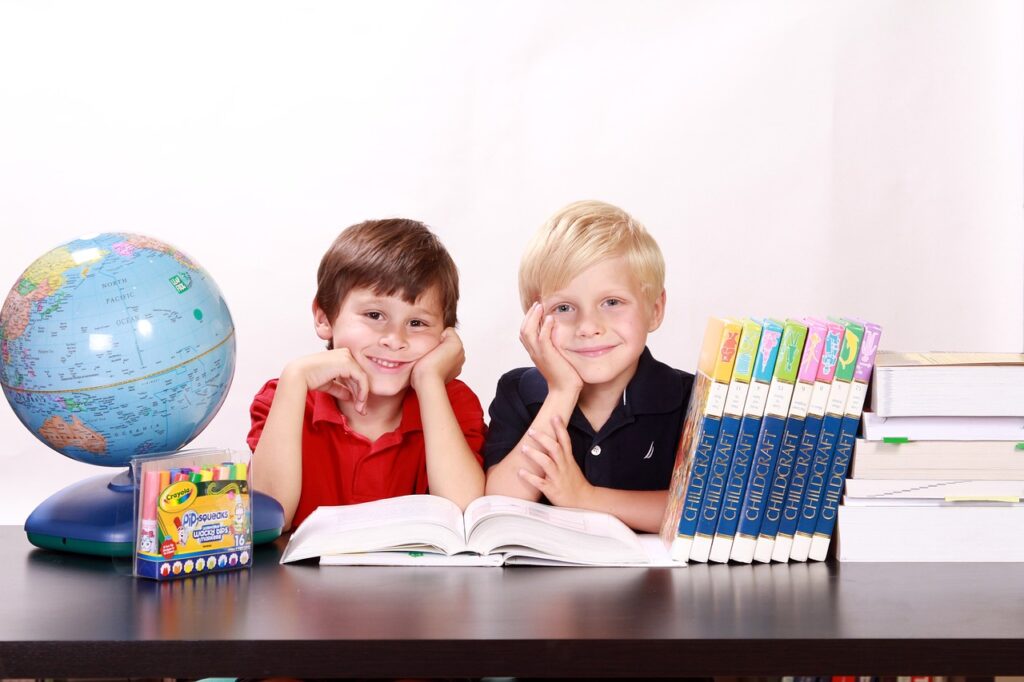 2 Kids Smiling with hands on table with globe and books 